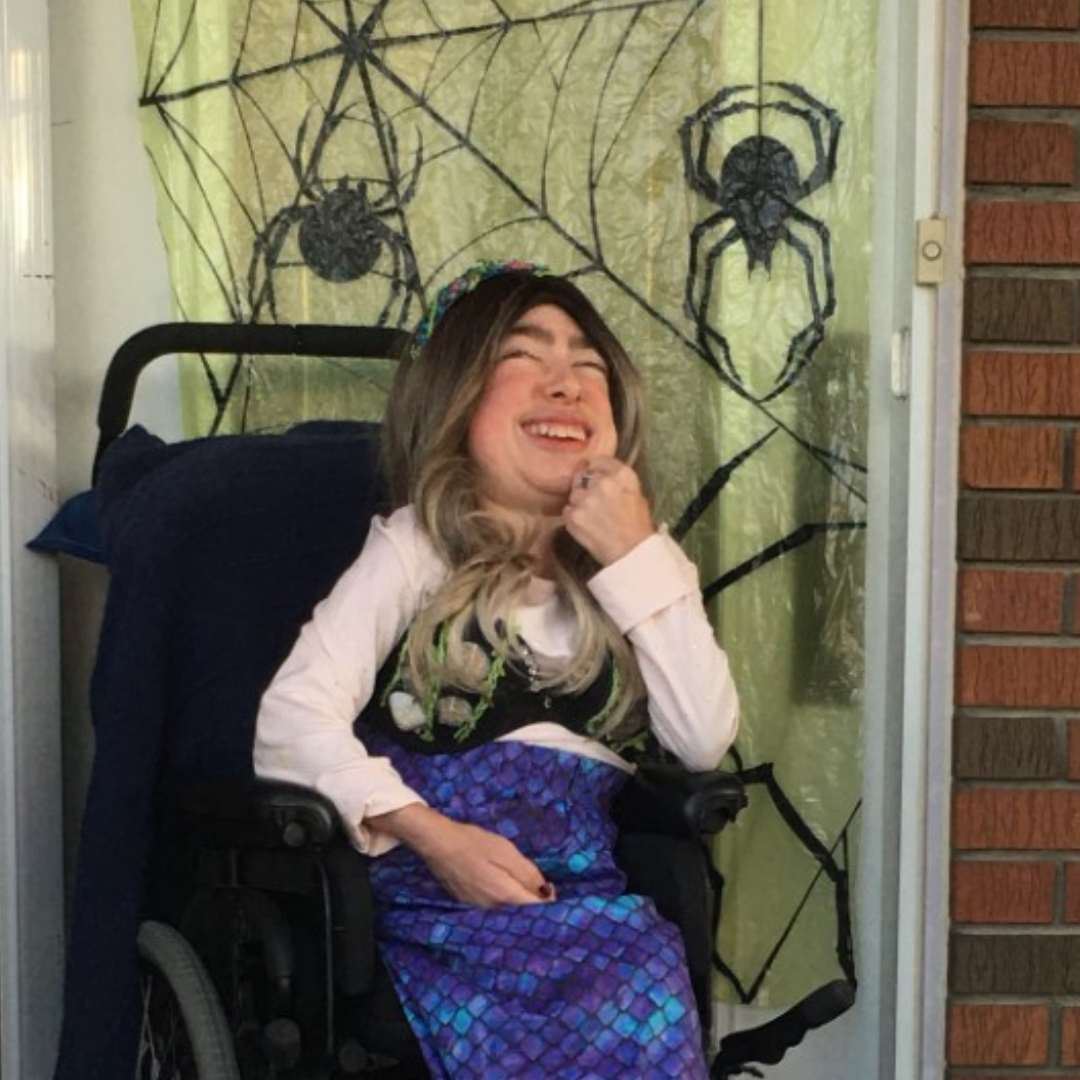 Monika sitting in her wheelchair outside her house at Halloween